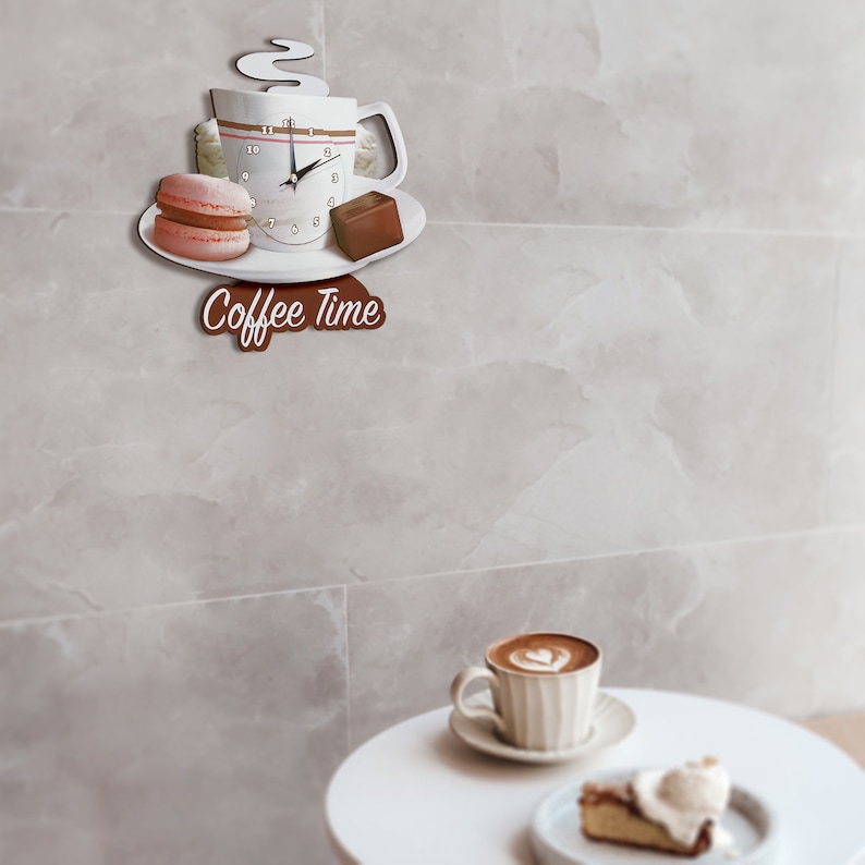 May include: White coffee cup clock with a macaron and chocolate bar on a white plate. The clock has a brown face with black hands and black numbers. The clock is hanging on a white tiled wall. The text "Coffee Time" is written in brown on a wooden sign below the clock.