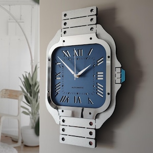 May include: A wall clock designed to resemble a wristwatch. The clock features a square blue face with white Roman numerals and hands. The clock's frame and band are silver-colored, with the word "AUTOMATIC" printed on the face.