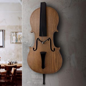 May include: A wooden wall clock shaped like a cello. The clock has a light brown body with black accents, including the strings, bridge, and scroll. The clock hands are black, and the clock is mounted on a gray wall.