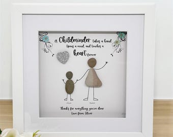 May include: Framed artwork with a white border. The artwork features a pebble art design of two figures holding hands, with the text "a Childminder takes a hand, Opens a mind, and touches a heart forever." Below are the names "Oliver" and "Rachel".