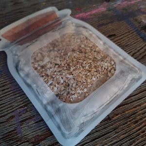 May include: A clear plastic jar with a brown lid, filled with a light brown, crumbly substance. The jar is sitting on a wooden surface.