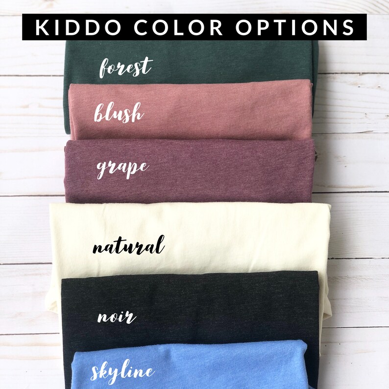 May include: A stack of folded fabric in various colors, including forest green, blush, grape, natural, noir, and skyline blue. The text "Kiddo Color Options" is at the top. Each color is labeled with a handwritten font.