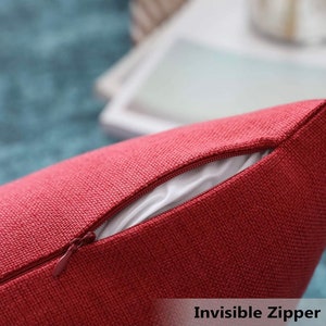 May include: A deep red throw pillow cover featuring a textured, woven fabric finish. The cover includes a matching red invisible zipper closure along the seam, which is partially open to reveal a smooth, white inner lining material inside.