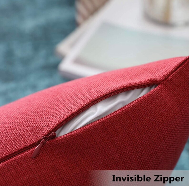 May include: A deep red throw pillow cover featuring a textured, woven fabric finish. The cover includes a matching red invisible zipper closure along the seam, which is partially open to reveal a smooth, white inner lining material inside.