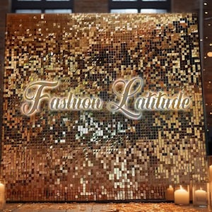 May include: A gold sequin backdrop with the text "Fashion Latitude" in white lettering.
