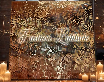 Könnte beinhalten: Ein goldfarbener Pailletten-Hintergrund mit dem Text "Fashion Latitude" in weißer, kursiv geschriebener Schrift. Der Hintergrund ist von Kerzen auf einer Holzoberfläche umgeben.