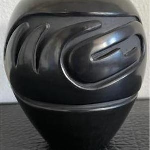 May include: A black ceramic pot with a rounded shape and a carved, wave-like pattern. The pot has a glossy finish and a slightly tapered base. The carved design creates a textured surface. The pot is likely for decorative purposes and is made of ceramic.