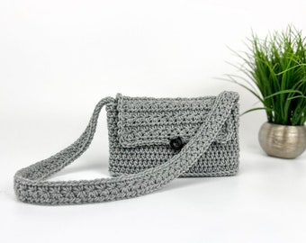 May include: A grey crocheted crossbody bag with a flap closure and a single button. The bag has a long strap and is made with a textured stitch.
