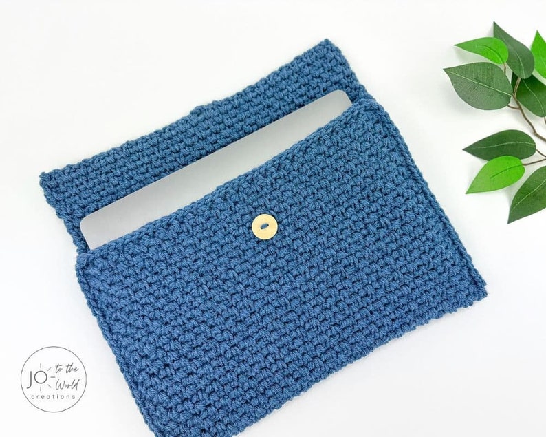 May include: A blue crocheted laptop sleeve with a wooden button closure. The sleeve is open and a laptop is inside.