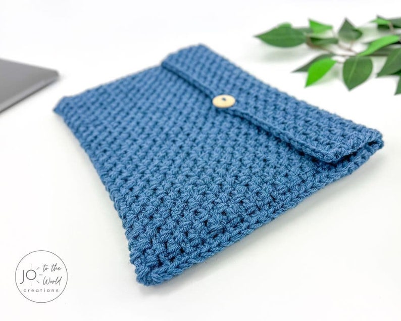 May include: A blue crocheted envelope clutch with a wooden button closure. The clutch is made with a textured stitch and is ideal for carrying small items.