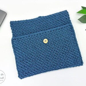 May include: A blue crocheted laptop sleeve with a button closure. The sleeve is made with a textured stitch pattern.