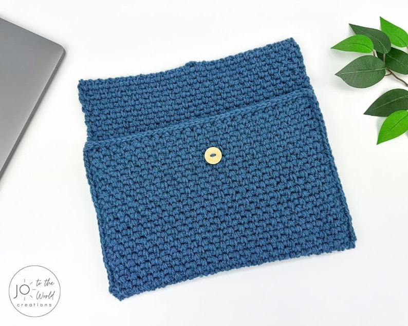 May include: A blue crocheted laptop sleeve with a button closure. The sleeve is made with a textured stitch pattern.