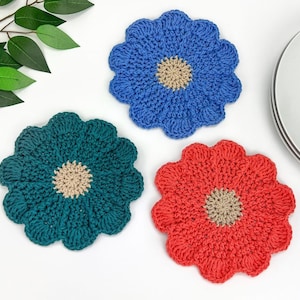 May include: Three crocheted flower-shaped coasters in teal, blue, and coral colors. Each coaster has a beige center.