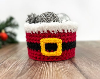 May include: A red and white crocheted Santa Claus-themed basket with a black belt and yellow buckle. The basket is filled with silver decorative balls.