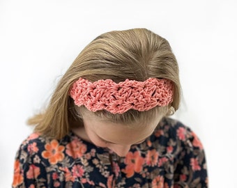 Könnte beinhalten: Ein rosa gehäkeltes Stirnband mit einem geflochtenen Design. Das Stirnband wird von einer Person mit langen blonden Haaren getragen.