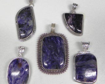 May include: Five silver-toned pendants with polished, marbled purple stones. The pendants vary in shape, including oval, rectangular, and asymmetrical designs. Each pendant has a silver bail for a chain.