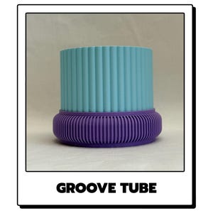 May include: A cylindrical object labelled GROOVE TUBE featuring a light blue upper section with vertical ridges and a purple lower base with a rounded, ribbed design. The object has a distinct two-tone colour scheme and a textured surface.
