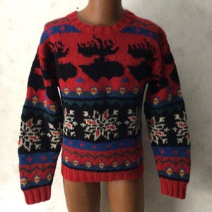 May include: A red crew-neck jumper with a black moose pattern on the chest. The jumper features a patterned design with blue, green, and white accents. The cuffs and hem are solid red.