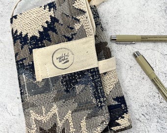 May include: A fabric pen case with a handle, featuring a geometric pattern in beige, navy, and brown. The case has a flap with the text "wishful usha" and includes two pens.