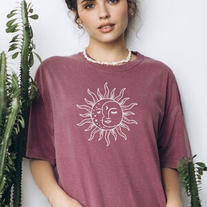 May include: A mauve oversized t-shirt with a white sun and moon graphic. The text "Berry" is printed on the bottom of the shirt.