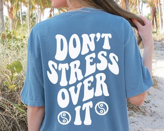 May include: A blue jean oversized t-shirt with white text that reads "Don't Stress Over It" with a yin yang symbol on either side of the word "It".