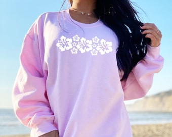 May include: A light pink sweatshirt with a white hibiscus flower design on the front.