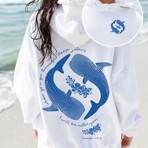 K&ouml;nnte beinhalten: Ein wei&szlig;er Kapuzenpullover mit einer blauen Grafik auf der R&uuml;ckseite, die zwei Walhaie in einem Kreis mit Blumenmotiven und dem Text "when you go through deep waters I will be with you. Isaiah 43:2" zeigt. Ein kleines passendes Logo ist vorne.