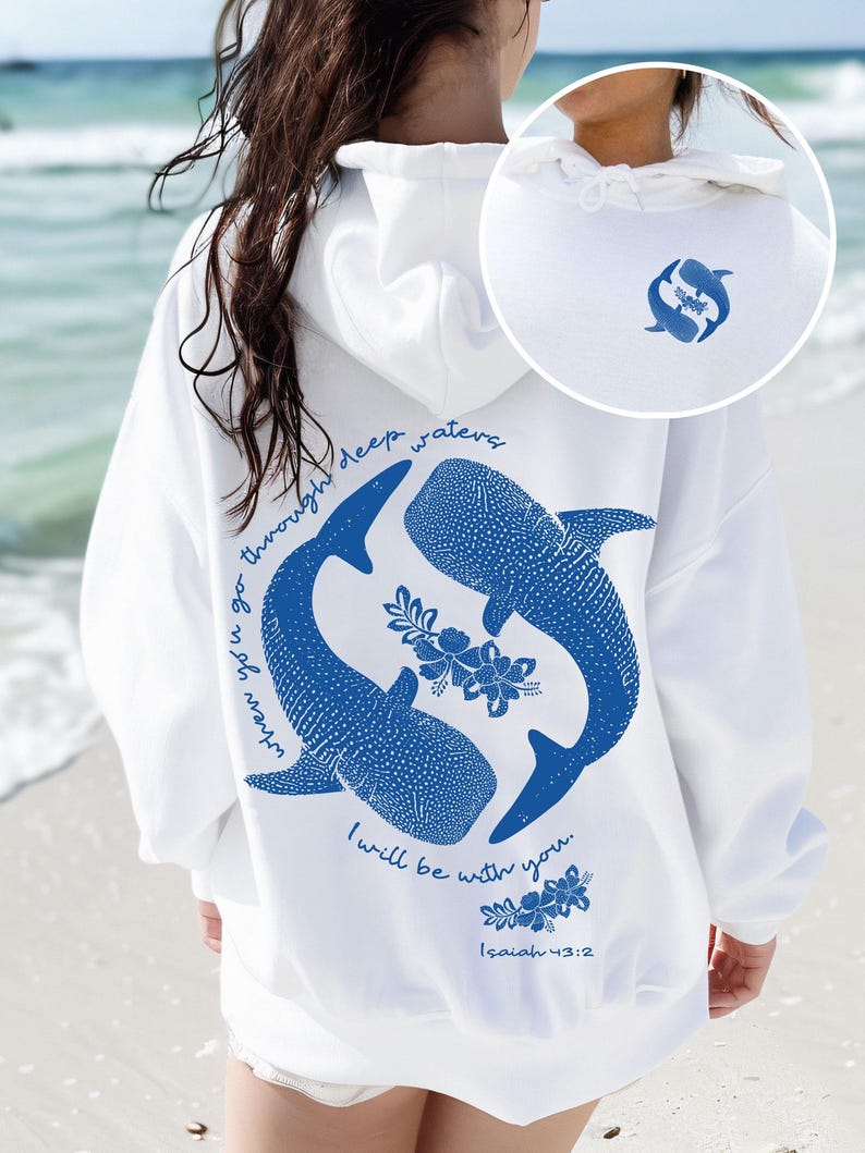 K&ouml;nnte beinhalten: Ein wei&szlig;er Kapuzenpullover mit einer blauen Grafik auf der R&uuml;ckseite, die zwei Walhaie in einem Kreis mit Blumenmotiven und dem Text "when you go through deep waters I will be with you. Isaiah 43:2" zeigt. Ein kleines passendes Logo ist vorne.