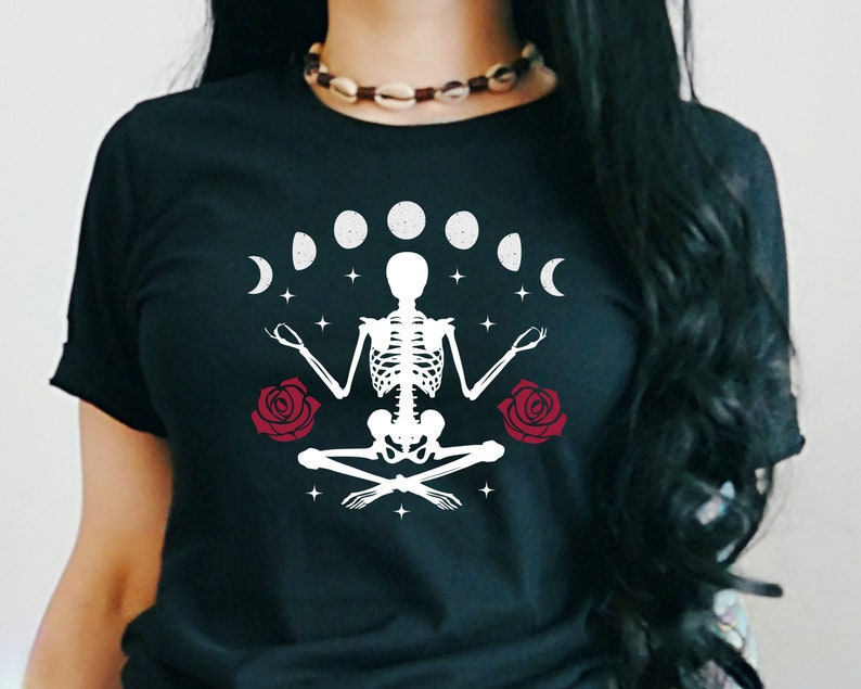 May include: Black t-shirt with a white skeleton meditating with a crescent moon and full moon phases above it. There are two red roses on either side of the skeleton. The text "Death is just a new beginning" is printed on the shirt.