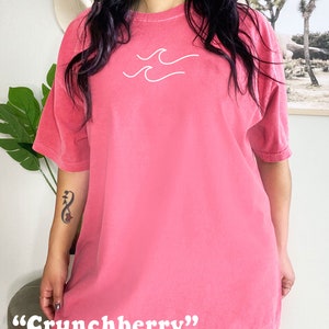 May include: An oversized pink t-shirt with a white wave graphic and the text "Crunchberry" printed on the bottom hem.