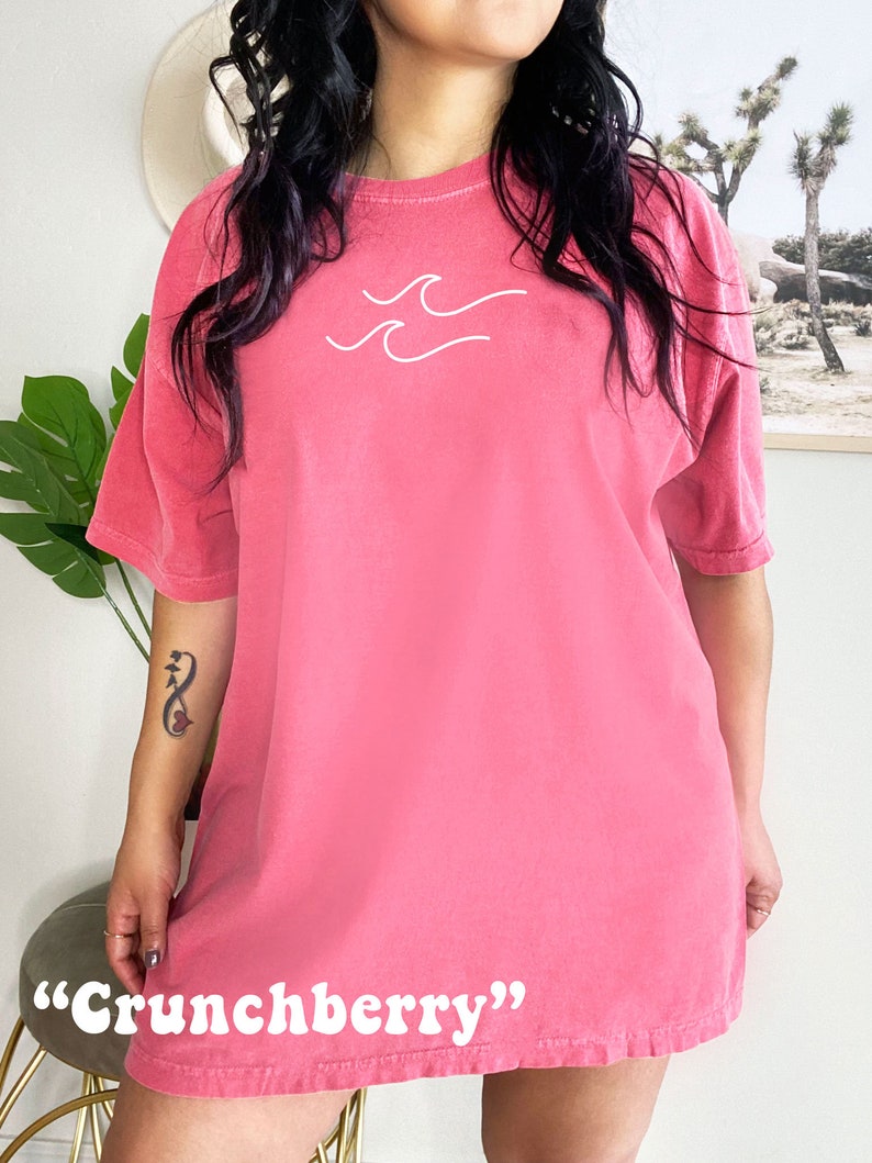 May include: An oversized pink t-shirt with a white wave graphic and the text "Crunchberry" printed on the bottom hem.