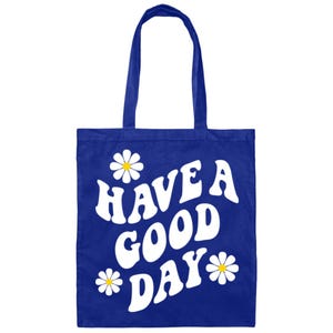May include: A royal blue tote bag with white daisies and the text "HAVE A GOOD DAY" in a retro font.