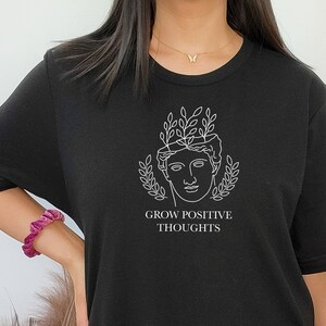 May include: Black t-shirt with a white graphic of a woman's head with leaves growing from it. The text "Grow Positive Thoughts" is below the graphic.