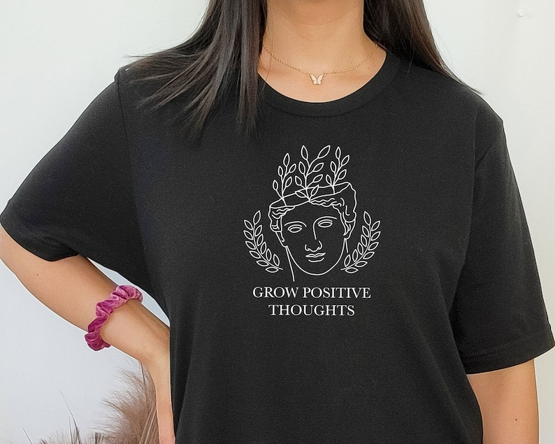 May include: Black t-shirt with a white graphic of a woman's head with leaves growing from it. The text "Grow Positive Thoughts" is below the graphic.