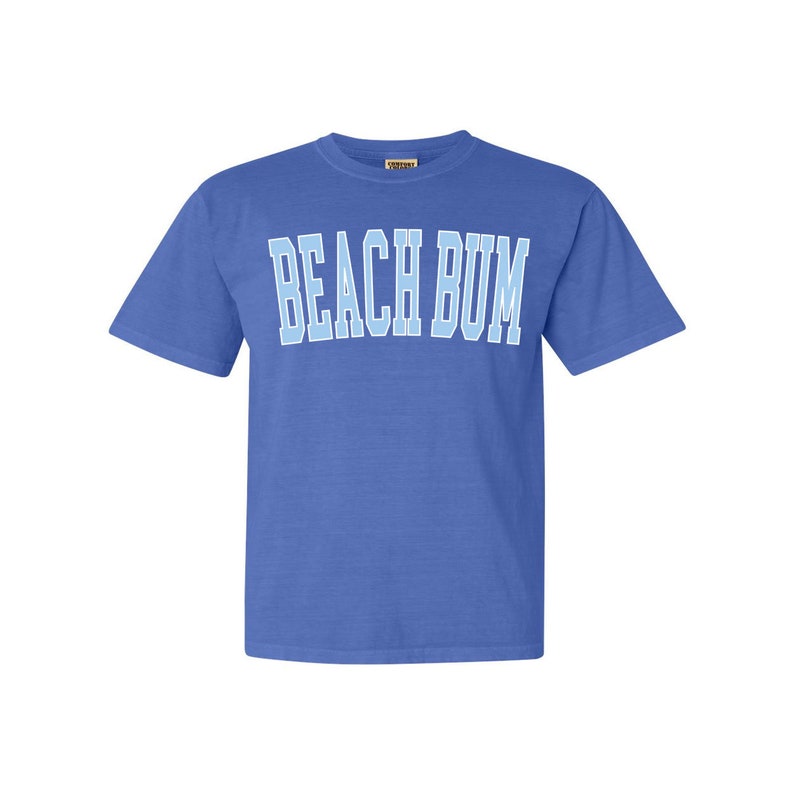 Pu&ograve; includere: Una t-shirt a maniche corte blu reale con il testo "BEACH BUM" in azzurro.