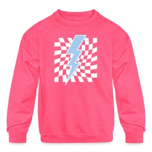 Puede incluir: Una sudadera rosa con un gr&aacute;fico de rayo azul sobre un fondo de cuadros blancos.