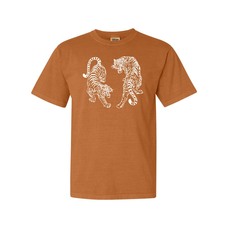 May include: A brown t-shirt with a white graphic of two tigers facing each other.