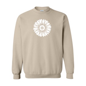Pu&ograve; includere: Una felpa beige con una grafica di girasole bianca sul davanti.