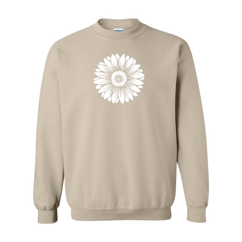 Pu&ograve; includere: Una felpa beige con una grafica di girasole bianca sul davanti.