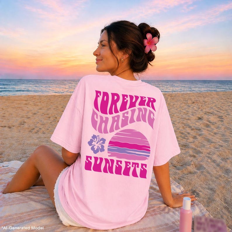 Pode incluir: Uma t-shirt de manga curta cor-de-rosa claro com um gr&aacute;fico nas costas que apresenta o texto "FOREVER CHASING SUNSETS" em letras onduladas cor-de-rosa e roxas, acompanhado por uma flor de hibisco roxa e um design circular de p&ocirc;r do sol.