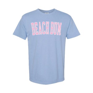May include: A light blue t-shirt with the text "BEACH BUM" printed in pink.