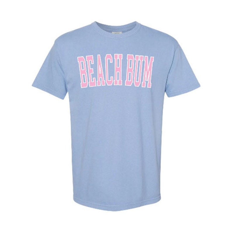May include: A light blue t-shirt with the text "BEACH BUM" printed in pink.