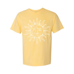 K&ouml;nnte beinhalten: Ein gelbes T-Shirt mit kurzen &Auml;rmeln und einem wei&szlig;en Sonnen- und Mondmotiv. Sonne und Mond k&uuml;ssen sich und haben ein Gesicht.