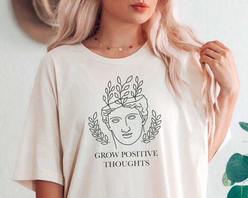 May include: White t-shirt with a black line drawing of a person's head with leaves growing out of it. The text "GROW POSITIVE THOUGHTS" is printed below the drawing.