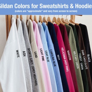 Pu&ograve; includere: Una fila di felpe e felpe con cappuccio Gildan in vari colori, tra cui bianco, cenere, grigio sportivo, sabbia, rosa chiaro, blu chiaro, blu Carolina, blu navy, heliconia (rosa acceso), marrone, verde militare, verde bosco, cioccolato scuro e nero.