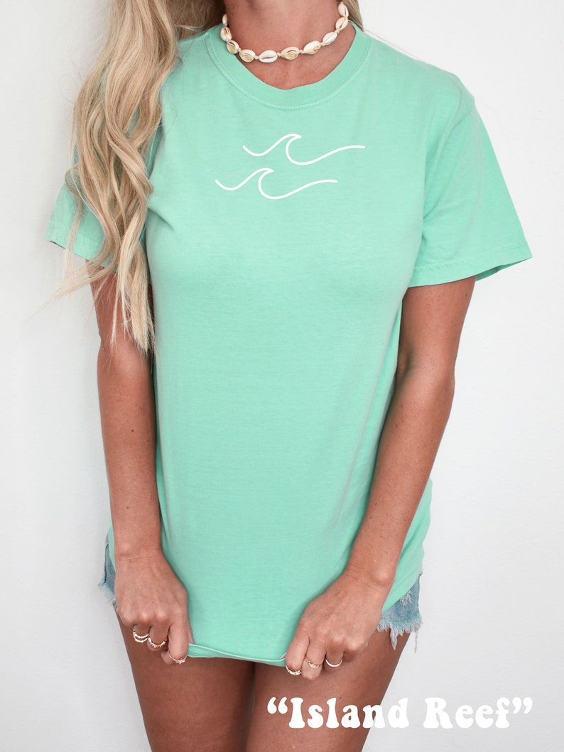 May include: A light green t-shirt with a white wave design and the text "Island Reef" printed on the bottom.