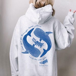 K&ouml;nnte beinhalten: Ein hellgrauer Kapuzenpullover mit einer blauen Grafik auf der R&uuml;ckseite. Das Design zeigt zwei Walhaie, die im Kreis schwimmen, umgeben von floralen Akzenten und dem Text: When you go through deep waters I will be with you. Isaiah 43:2.