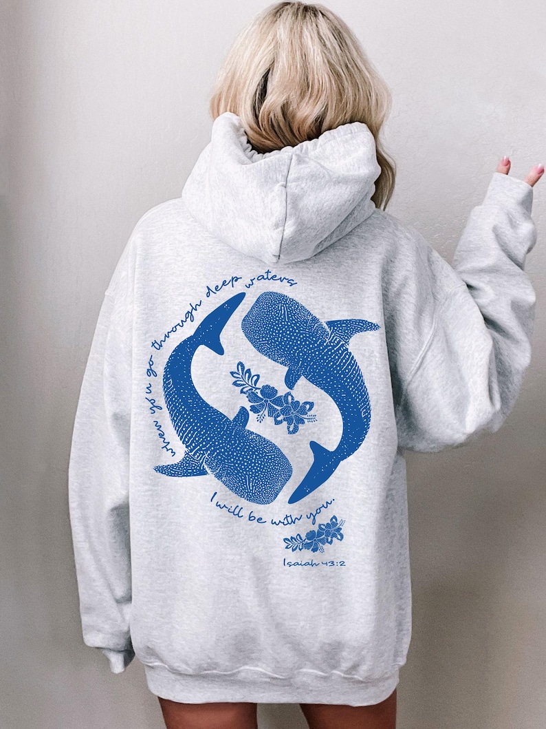 K&ouml;nnte beinhalten: Ein hellgrauer Kapuzenpullover mit einer blauen Grafik auf der R&uuml;ckseite. Das Design zeigt zwei Walhaie, die im Kreis schwimmen, umgeben von floralen Akzenten und dem Text: When you go through deep waters I will be with you. Isaiah 43:2.
