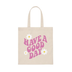 May include: A beige tote bag with pink text that reads "HAVE A GOOD DAY" and three white daisies with yellow centers.