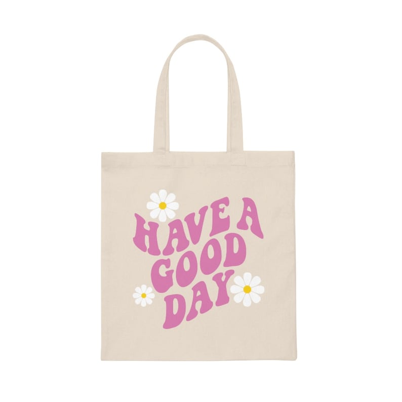 May include: A beige tote bag with pink text that reads "HAVE A GOOD DAY" and three white daisies with yellow centers.